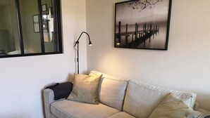 A beige sofa with multiple cushions, a black floor lamp, and a framed picture of a bridge on the wall.