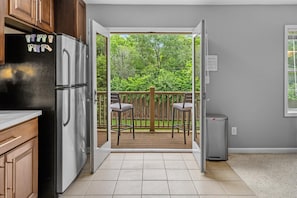 A kitchen with a refrigerator, a dining area with chairs, a wooden deck, and a view of greenery. - DT Indy near Convention Center (Indianapolis)
