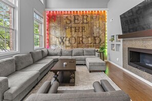 A modern living room with a sectional sofa, a coffee table, a fireplace, and a large wall mural. - DT Indy near Convention Center (Indianapolis)