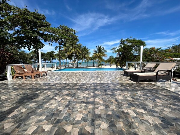 A pool area with stone flooring, lounge chairs, and palm trees.