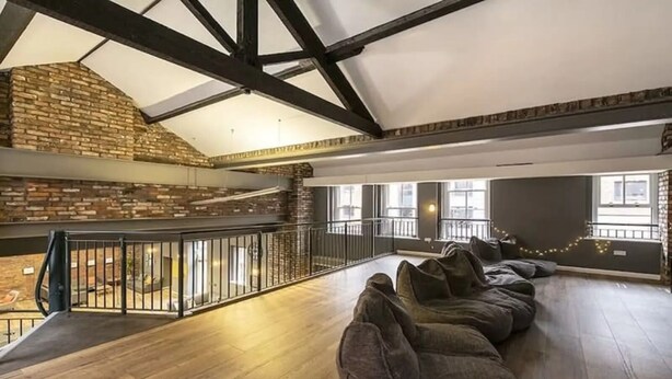 Un vaste espace de vie de style loft, avec des murs en briques apparentes, un plancher en bois et une mezzanine dotée d’un balcon.