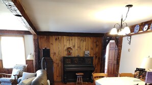 Een rustieke kamer met houten vloer, een piano, een eettafel met stoelen en een bank.