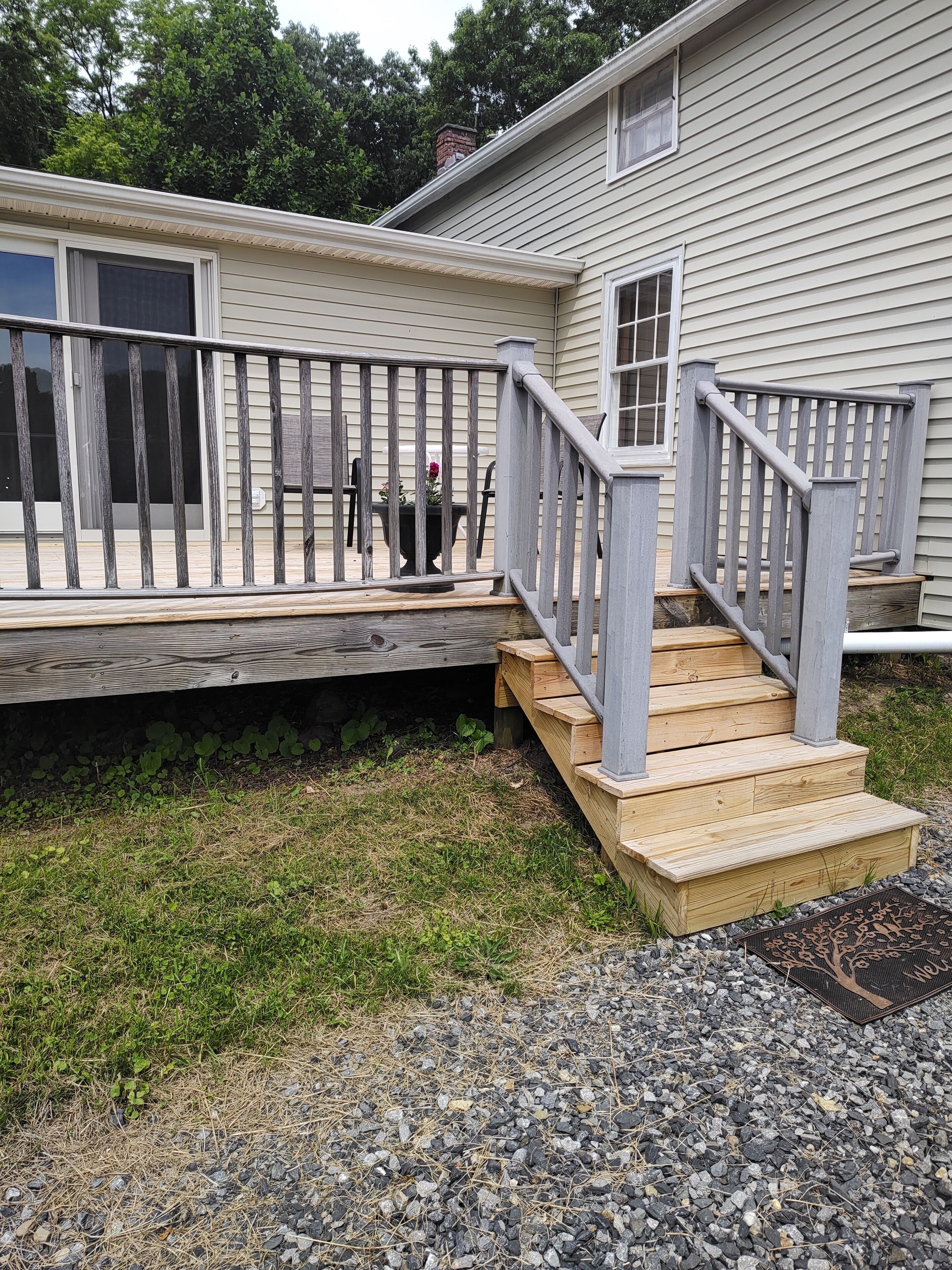 A residential house with a wooden deck, a grey staircase, and a small front porch.