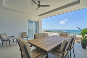 A balcony with a wooden table and chairs, a ceiling fan, and a view of the ocean.