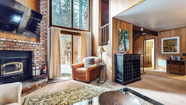 Un salon chaleureux avec une cheminée, un canapé en cuir et une grande fenêtre donnant sur les arbres.