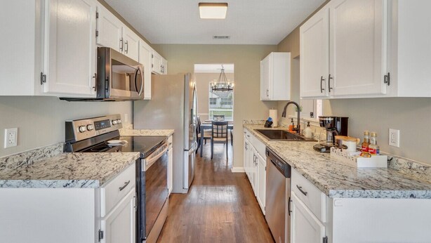 A kitchen with white cabinets, a stainless steel range, a dishwasher, and a granite countertop.