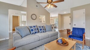 A living room with a sofa, blue chair, wooden coffee table, and ceiling fan.