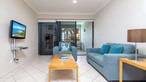 A modern living room with a flat-screen TV, a wooden coffee table, a blue sofa, and a lamp.