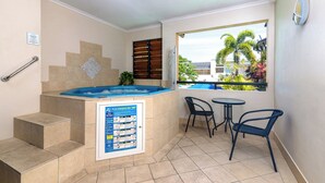 A bathroom with a hot tub, a poster, a window with a view of palm trees, and a small table with chairs.