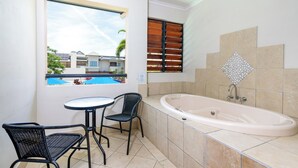 Un baño con bañera, una ventana con persianas y una pequeña mesa con sillas.