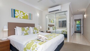 Una habitación de hotel con una cama grande, una mesita de noche con l ámpara, un ventilador de techo, un equipo de aire acondicionado y un espejo amplio.
