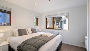 A bedroom with a large bed, a bedside table, a mirror, and windows.
