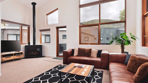 A modern living room with a fireplace, leather sofa, and large windows offering a view of the outdoors.