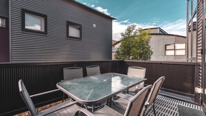 An outdoor patio with a glass-top table and metal chairs, surrounded by a metal fence.
