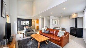 A spacious living room with a leather sofa, a wooden coffee table, and a fireplace. - Snow Stream 5 a 2 bedroom & loft apartment close to Friday Flat. (Thredbo)