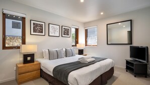 A modern bedroom with a large bed, bedside lamps, a TV, and framed artwork on the walls. - Snow Stream 5 a 2 bedroom & loft apartment close to Friday Flat. (Thredbo)
