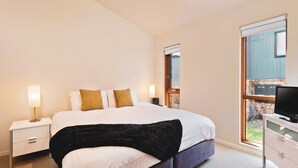A hotel room with a bed, bedside tables, a TV, and a large window with a view of the outside.