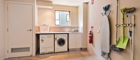 Een wasruimte met twee wasmachines, een brandblusser en schoonmaakmiddelen aan de muur.
