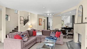 A modern living room with a sectional sofa, a glass coffee table, and a dining area with chairs and a table. - Village Green Townhouse 2 bedrooms and loft with spectacular views, garage parking and a wood fire. (Kosciuszko National Park)