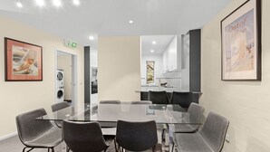 A conference room with a glass table, six chairs, a kitchen area, and a framed picture on the wall. - Village Green Townhouse 2 bedrooms and loft with spectacular views, garage parking and a wood fire. (Kosciuszko National Park)