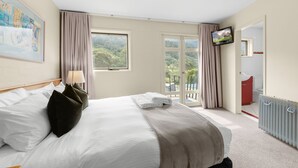 A hotel room with a bed, a TV, a balcony, and a bathroom. - Village Green Townhouse 2 bedrooms and loft with spectacular views, garage parking and a wood fire. (Kosciuszko National Park)