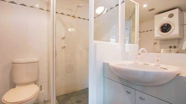 Un baño moderno con inodoro, ducha, lavamanos y lavadora integrada.