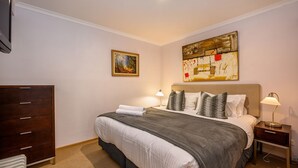 Un dormitorio ordenado con una cama grande, un aparador, dos mesitas de noche con lámparas y dos cuadros en las paredes.