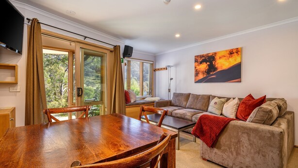 Una sala de estar acogedora con una mesa de comedor de madera, un sofá y un amplio ventanal con cortinas.