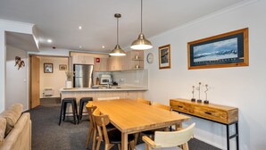 A modern kitchen with stainless steel appliances, a wooden dining table, and pendant lighting.