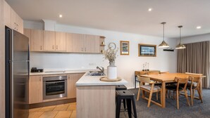 A modern kitchen with wooden cabinets, a stainless steel refrigerator, an oven, and a dining area with a wooden table and chairs.