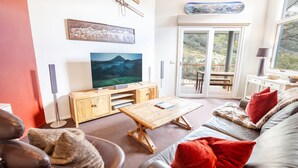 Una sala de estar con televisor, muebles de madera, un sofá con cojines rojos y un ventanal corredero que da a un patio exterior.
