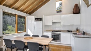 Une cuisine moderne avec des meubles blancs, une table à manger en bois et une grande fenêtre donnant sur un paysage verdoyant.