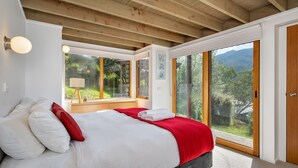 Une chambre à coucher comprenant un lit, une table de chevet, une lampe et une vue sur un paysage montagneux, visible à travers de grandes portes coulissantes en verre.