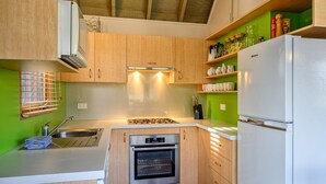 A compact kitchen with wooden cabinets, a built-in oven, a stainless steel sink, and a white refrigerator. - Banjo 5 - Two Bedroom & Loft Townhouse with mountain views (Thredbo)