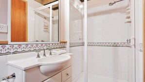 A bathroom with a white sink, two faucets, a mirror, and a shower with a glass door. - Banjo 5 - Two Bedroom & Loft Townhouse with mountain views (Thredbo)