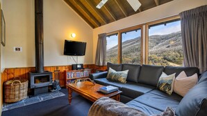 A cozy living room with a fireplace, a sofa, a coffee table, and a bookshelf. - Banjo 5 - Two Bedroom & Loft Townhouse with mountain views (Thredbo)
