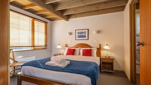 Een slaapkamer met een houten plafond, een bed met een blauwe deken, twee bedlampen en een ingelijst schilderij aan de muur.