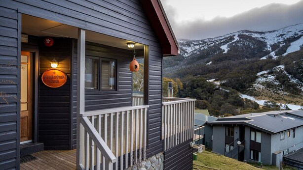 A dark wooden building with a balcony, a sign reading "Crockenburgh Castle," and a mountainous landscape in the background. - A stand alone 2 bedroom chalet with a large veranda to take in the mountain views (Thredbo)