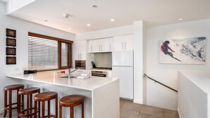 A modern kitchen with a central island, bar stools, a stove, and a refrigerator.