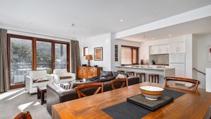 A spacious living room with a dining area, a kitchen, and large windows.