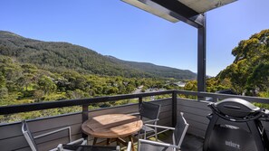 Un balcón con mesa y sillas de madera, con vistas a un paisaje montañoso.