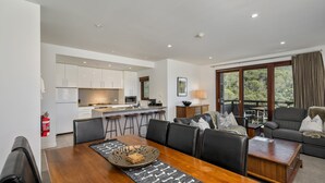 Una sala de estar moderna con comedor, cocina y un ventanal con vistas a árboles.