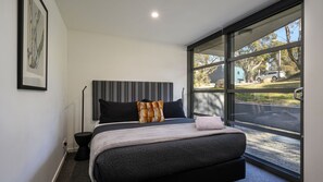 A modern bedroom with a large window, a bed with grey bedding, a black headboard, and a framed picture on the wall. - Pilot 1 Chalet an expansive open plan 3 level ski chalet (Thredbo)