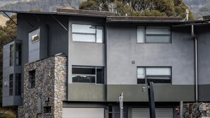 A modern two-story building with a stone facade, large windows, and a garage door. - Pilot 1 Chalet an expansive open plan 3 level ski chalet (Thredbo)