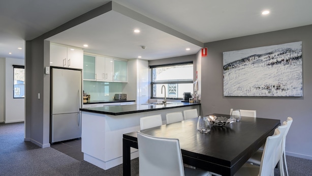 A modern kitchen with white cabinets, a black countertop, and a dining area with a black table and white chairs.