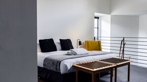 A modern hotel room with a bed, a bedside table, a chair, and a window.