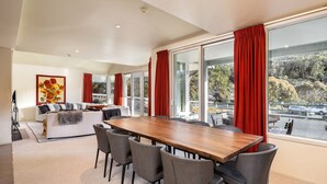 A spacious living area with a wooden dining table, grey chairs, a white sofa, and red curtains.