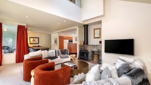 A spacious living room with a fireplace, a flat-screen TV, and a dining area with red curtains.