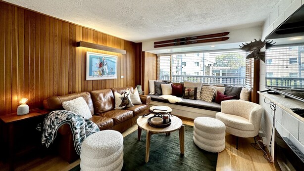 Una sala de estar acogedora con un sofá de cuero marrón, un sillón blanco y una mesa de centro de madera.