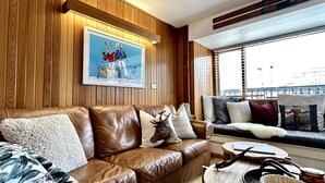 Una sala de estar moderna con un sofá de cuero, cojines decorativos, una obra de arte enmarcada y vistas de la ciudad a través de amplios ventanales.